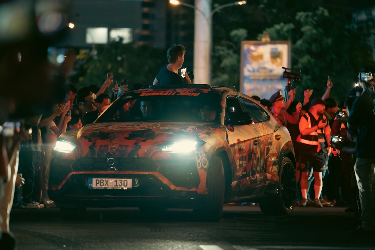A luxury SUV with orange graphics drives through a crowd.